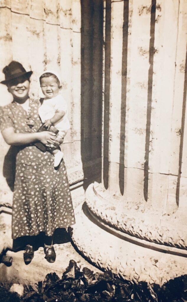 Itsuye Tsuchida standing next to a large column holding her young son at the Palace of Fine Arts in San Francisco.