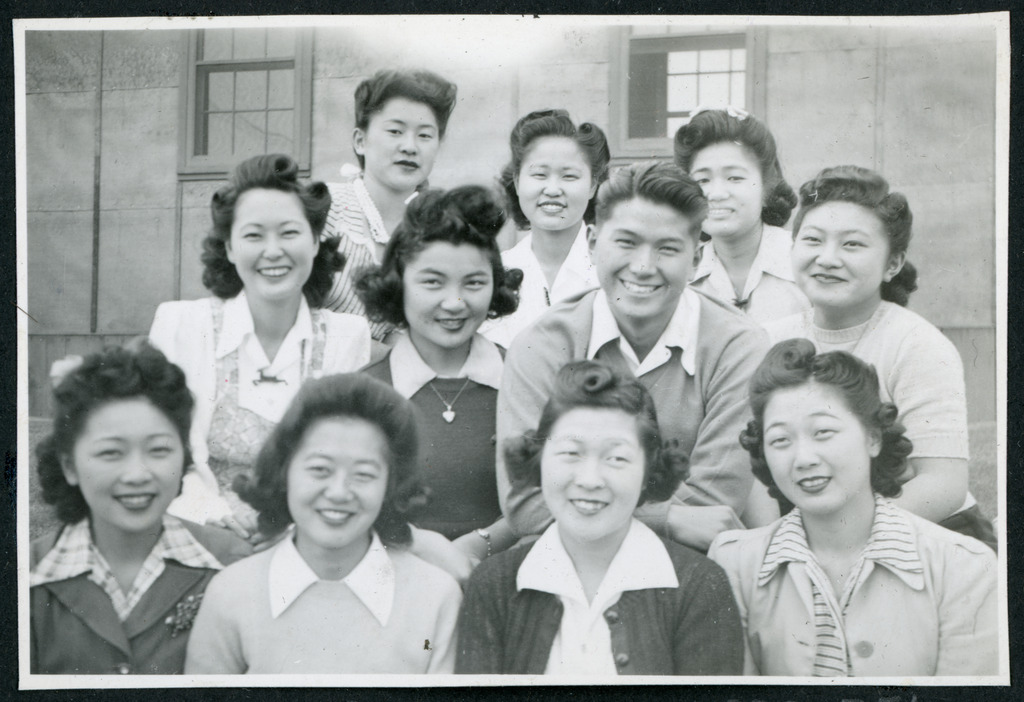 A group of young adult friends smiling and posing in front of a barrack in Manzanar concentration camp.