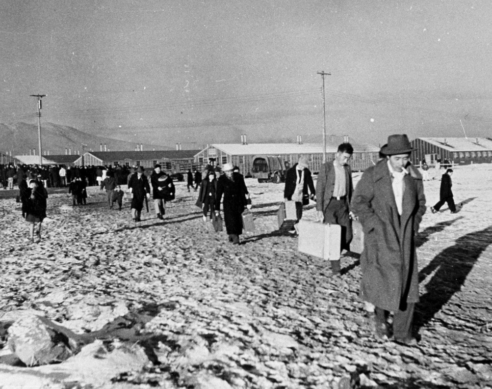 Japanese Americans walking through the snow carrying luggage at Tule Lake concentration camp. They are being transferred from Manzanar for their responses to the loyalty questionnaire.