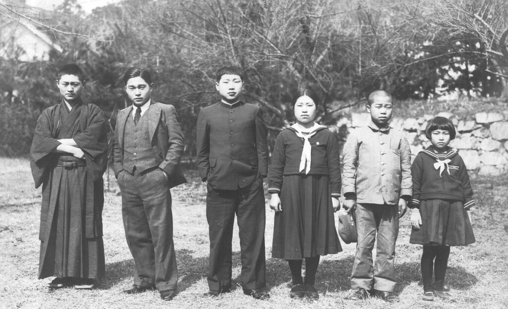 Six kibei siblings in Japan. They are standing in a row, one wearing dark colored hakama and haori, another in a western suit, and the four younger siblings in school uniforms.