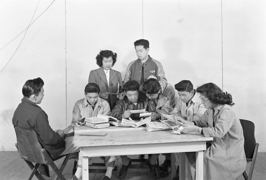 Japanese American teens gathered around a table reading at Minidoka