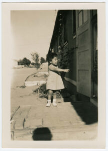A young Japanese American child pointing into the doorway of a barrack at Amache concentration camp.