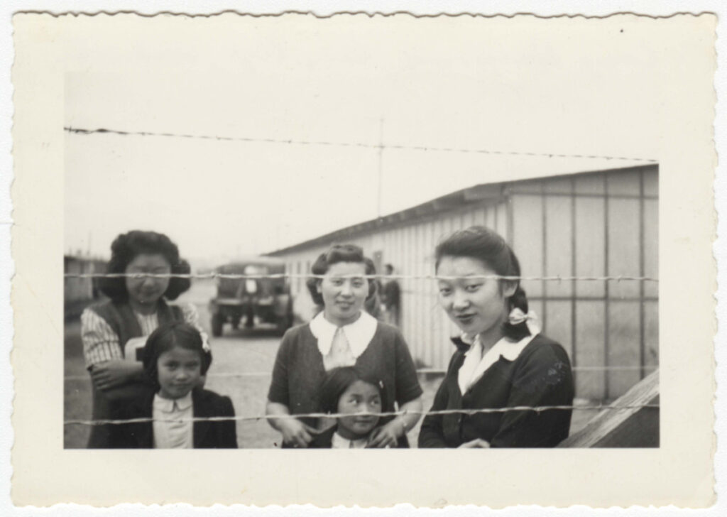 Three Japanese American women and two girls standing behind a fence at Puyallup Assembly Center in 1942.