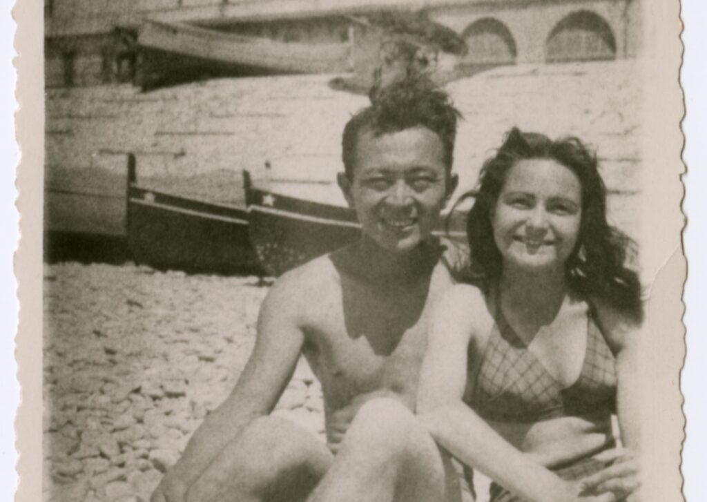 A Japanese American man and French woman sitting together at a beach in France circa 1944 to 1945.