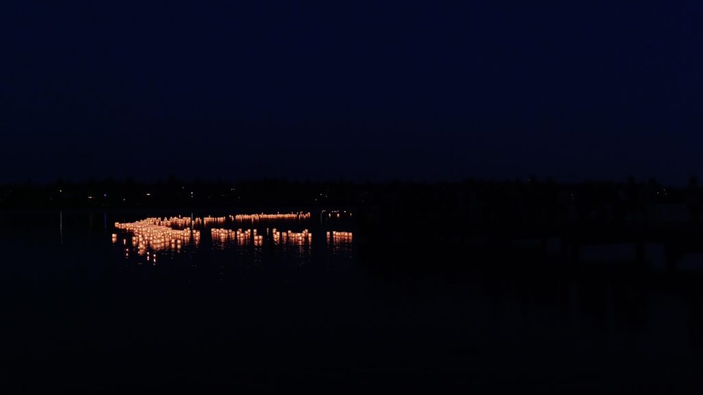 Candle lit lanterns floating on Seattle's Green Lake after dark at the 2024 From Hiroshima to Hope ceremony.