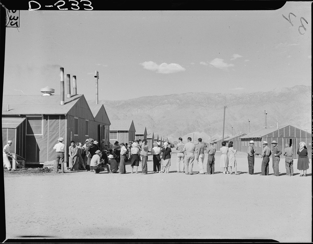 Japanese Americans lined up outside a concentration camp barracks waiting for a meal.