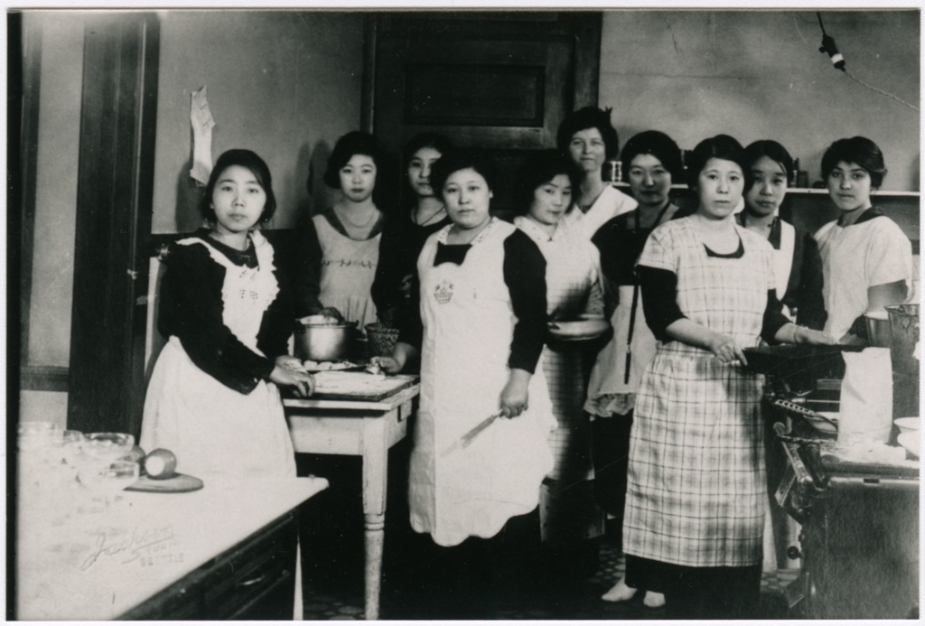 A group of Japanese American women participating in a cooking class at a women's home circa 1920.