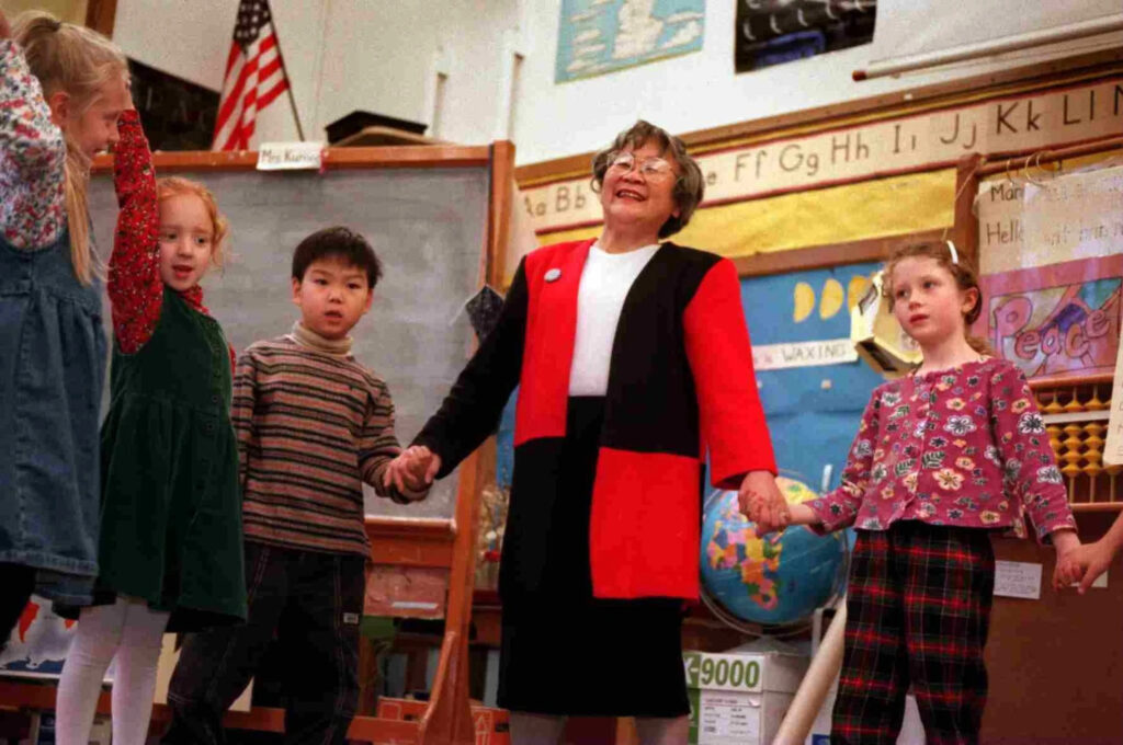 Aki Kurose holds hands with her young students inside her classroom.