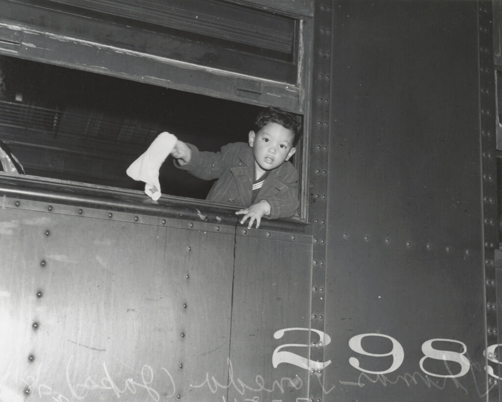 Three year old Tommy Yoneda leaning out a window waving goodbye on the train to Manzanar in 1942.