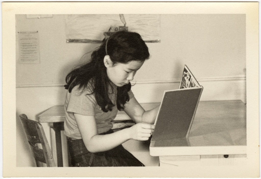 Japanese American girl sitting at a desk reading a book.