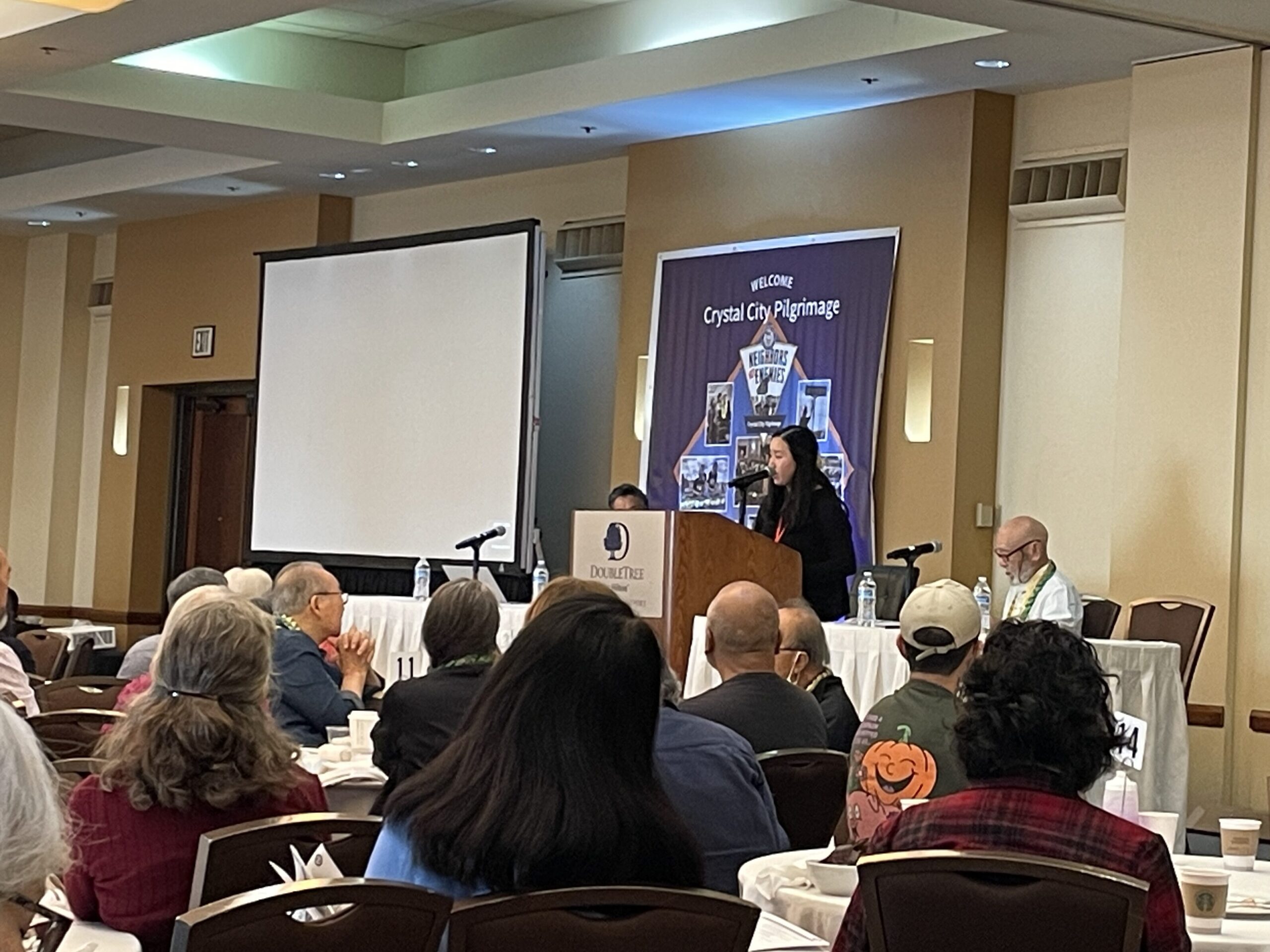 Pilgrimage co-chairs Hiroshi Shimizu, Brian Shibayama, and Gabi Nakashima sitting and speaking in front of crowd.