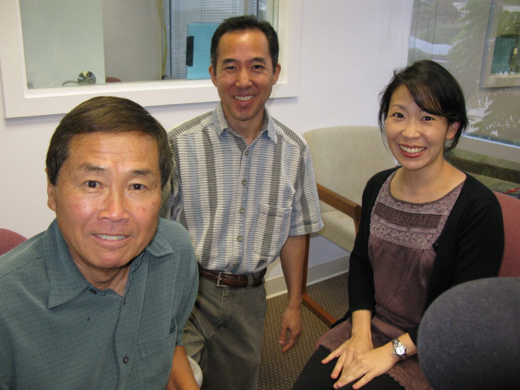 A photo of Dennis Ogawa, Brian Niiya, and Kelli Nakamura (left to right) smiling, taken during a radio show in 2010.