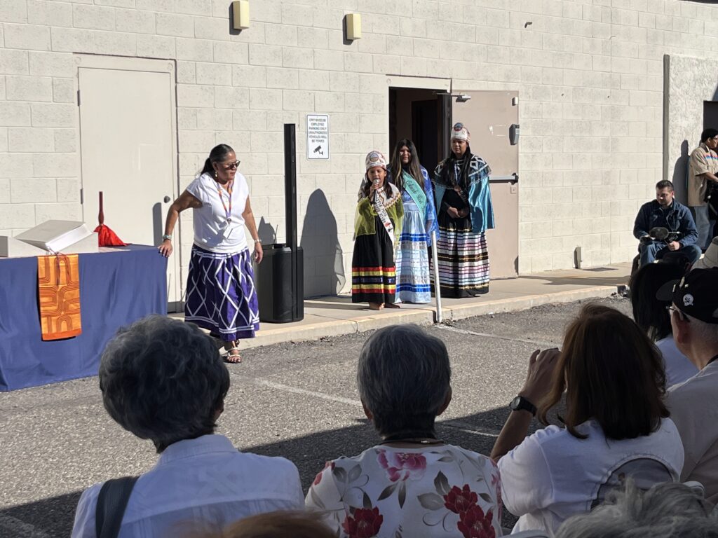Opening ceremony at CRIT Museum with the tribal community, with a moderator and three tribal community members in traditional clothing standing in a row. 