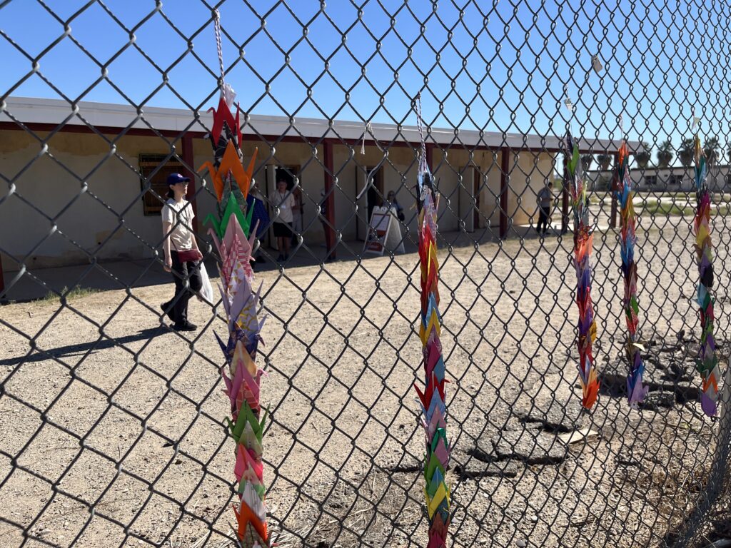 Paper cranes hang from a chain-linked fence at the remains of a Poston concentration camp elementary school site.