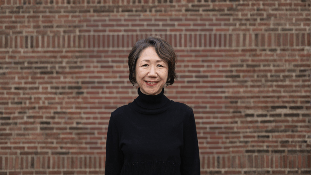 Naoko Tanabe smiling and standing in front of a brick wall