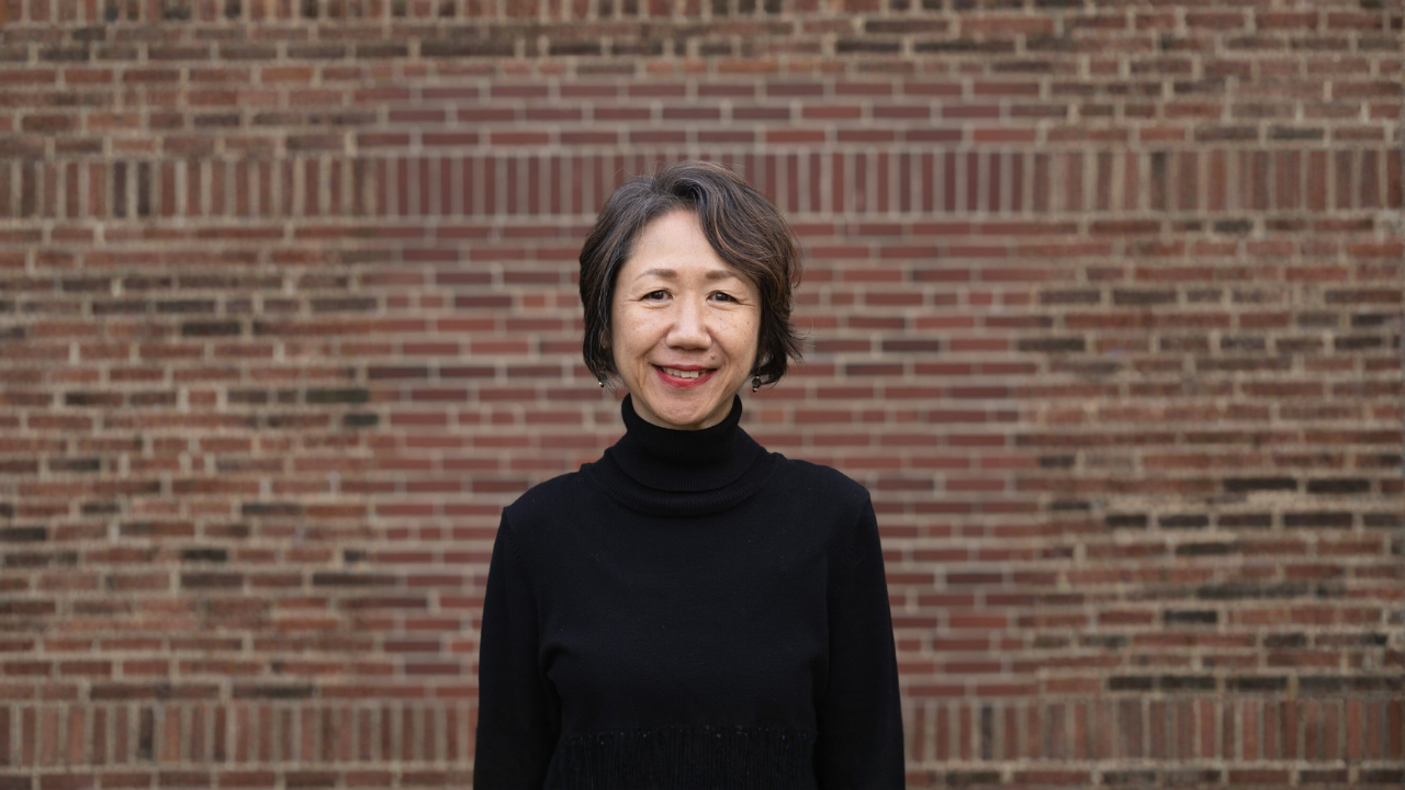 Naoko Tanabe smiling and standing in front of a brick wall