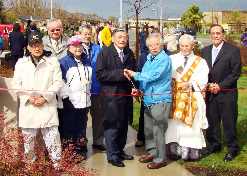 James Hirabayashi (third from right) and former Secretary of Transportation Norman Mineta (middle) cut the ribbon at a memorial plaza at the assembly center site in Fresno on Feb. 16, 2009. Photo by John Hix.