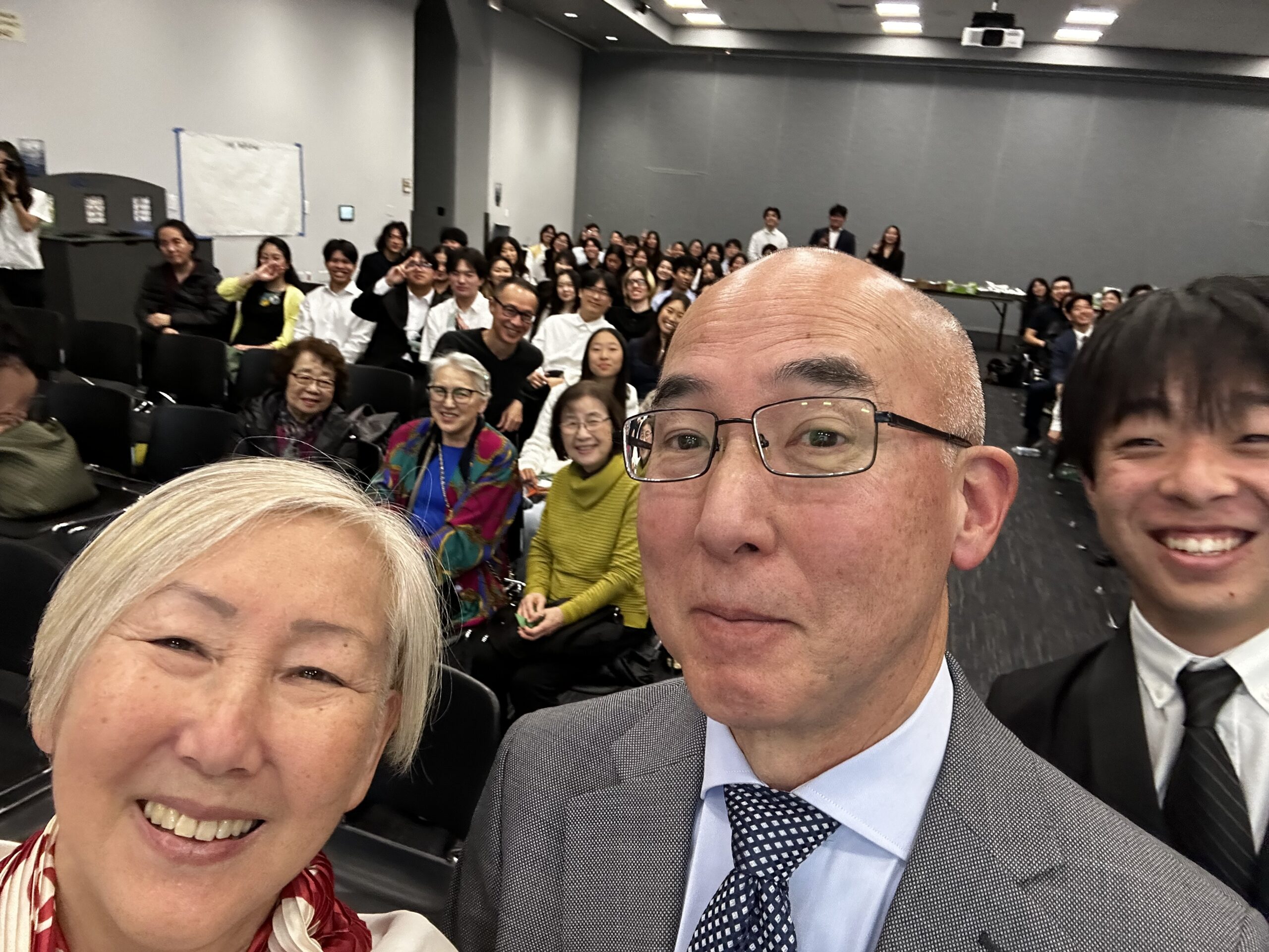 Selfie of Brian Niiya (front right) with Karen Umemoto (left) in front of attendees for UCI Tomo No Kai event. February 15, 2026, UC Irvine Student Center.