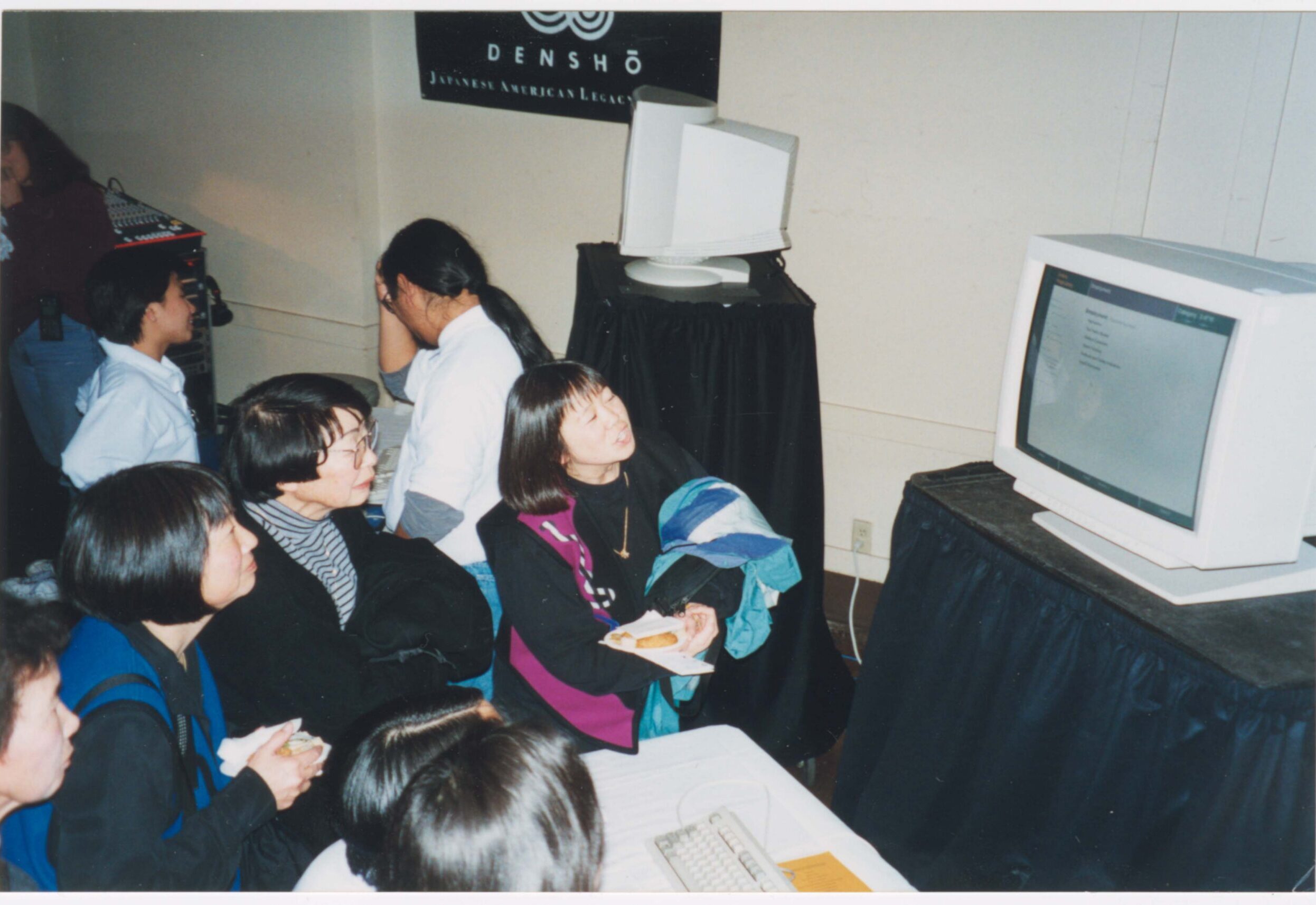 Densho Opening Gala attendees looking at Densho computer display with staff in the background.