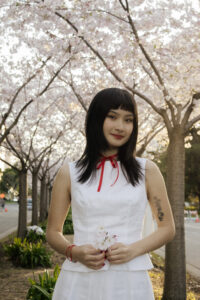 Amber Hisatomi headshot; Amber standing in front of cherry blossom trees