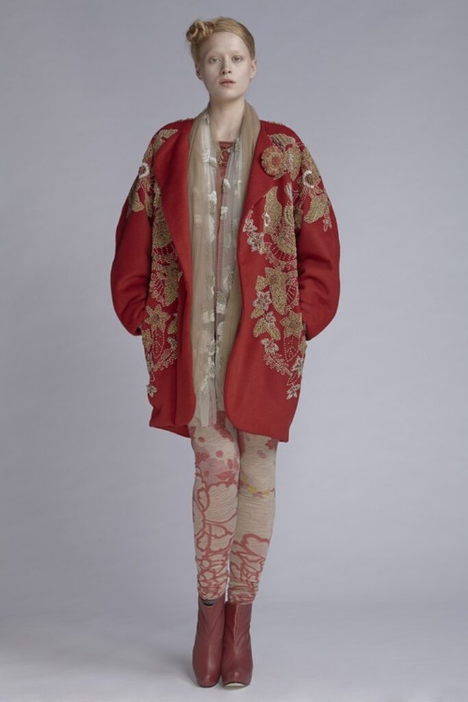 Photo of a pale blonde model wearing a modern deep orange red kimono outfit with beige leggings and small brown boots.