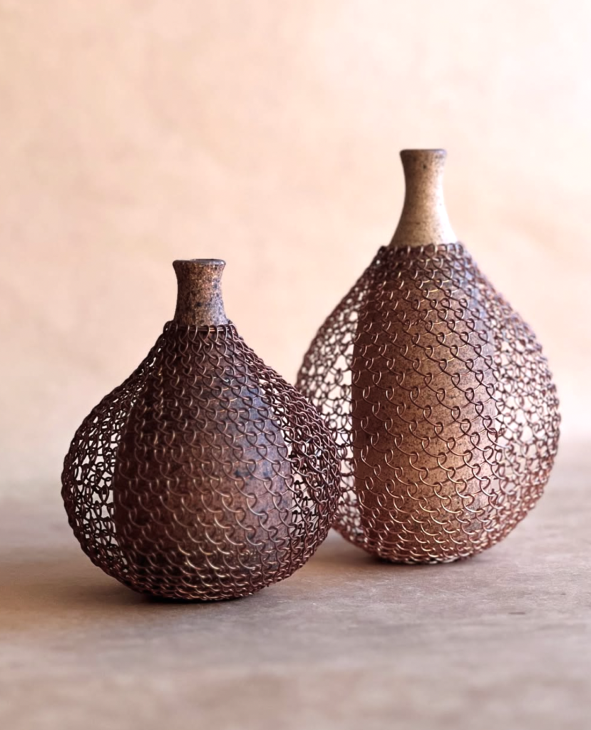 A photo of artwork. Two bottles, ceramic and looped copper wire on top.