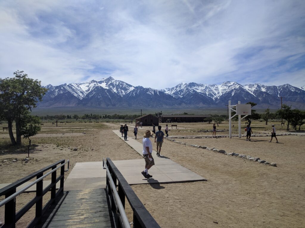 Ramp leading to the paved walkway at Manzanar with several visitors walking and mountains in the distance.