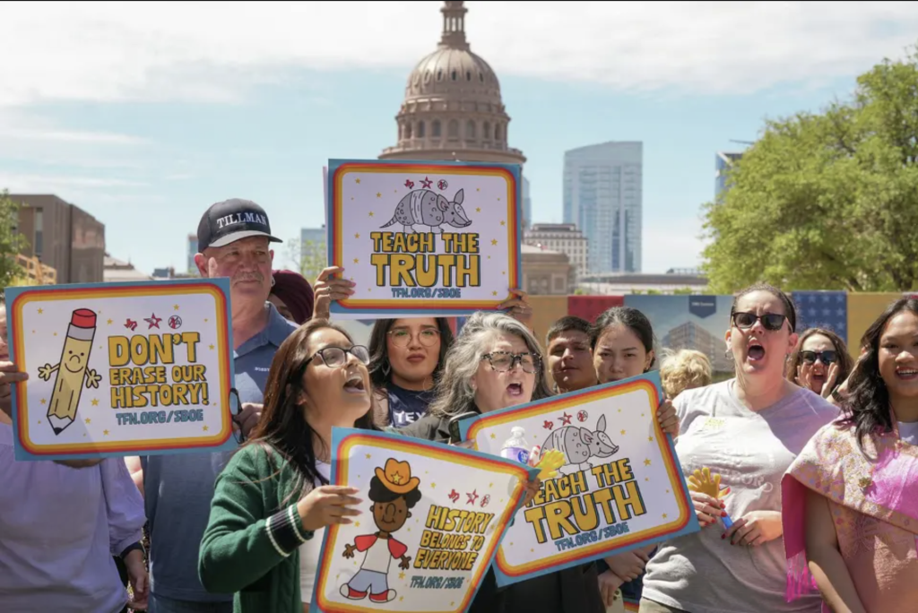 Diverse group of people hold signs reading “Teach the Truth” and “Don’t erase our history” during a rally on the Capitol Mall outside the Barbara Jordan State Office Building.