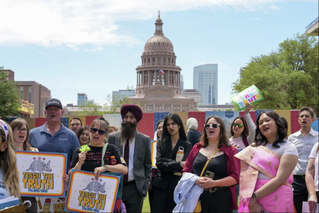 Diverse crowd of people holding signs reading “Teach the Truth” during a rally at the Capitol Mall outside the Barbara Jordan State Office Building.