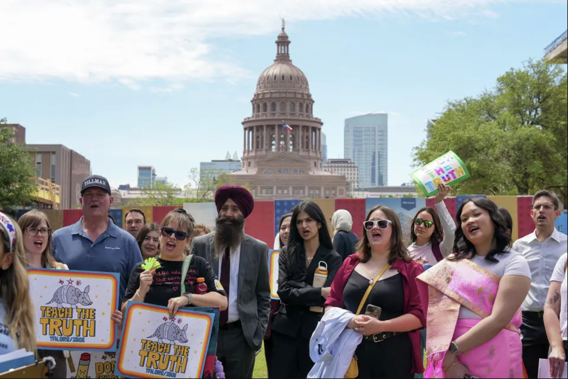 Diverse crowd of people holding signs reading “Teach the Truth” during a rally at the Capitol Mall outside the Barbara Jordan State Office Building.