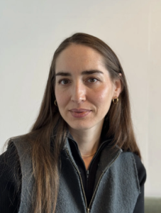 Headshot of Asian American woman with brown hair, gold hoop earrings, wearing a grey zip up vest and jacket.