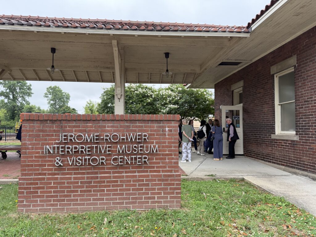 A group gathers at the entrance of a brick building with a sign reading "Jerome-Rohwer Interpretive Museum & Visitor Center."