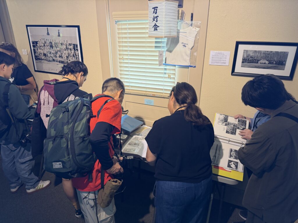 Several visitors look through binders of historical photographs and documents displayed on a table inside the museum, surrounded by framed archival photos on the walls.
