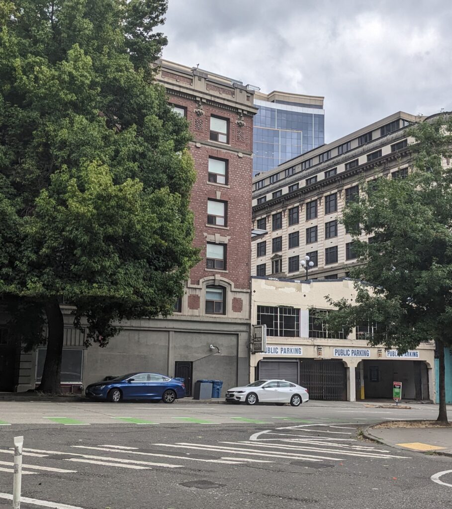 Contemporary photo of a city street showing two cars parked in front of a parking building under a brick building