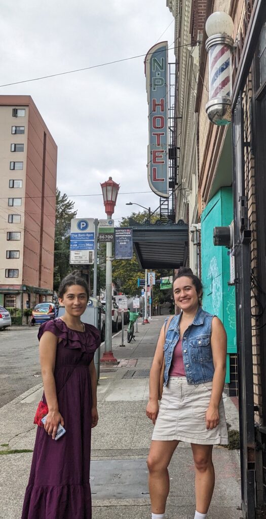 Color, contemporary photo of two women standing on city street in Seattle under NP Hotel sign