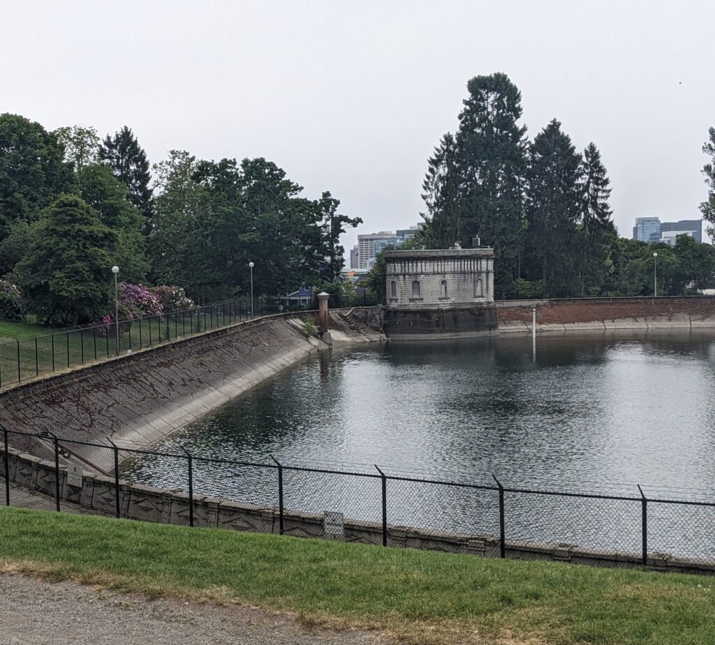 Photo of reservoir on a cloudy day. A fence and trees surround the water